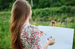 retrato de uma jovem atraente em vestido longo pintando com aquarela na natureza. foto