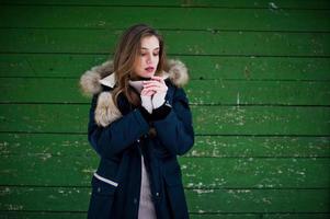 linda menina morena em roupas quentes de inverno. modelo na jaqueta de inverno contra fundo verde de madeira. foto