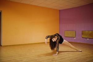 morena encaracolada mais modelo de tamanho fazendo acrobacias na sala de dança. foto