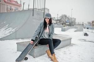 menina morena elegante boné cinza, estilo casual de rua com skate em dia de inverno. foto