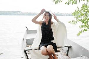 retrato de uma mulher feliz no vestido de bolinhas segurando um livro acima da cabeça enquanto está sentado em um barco velho. foto