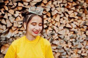 jovem garota engraçada com maquiagem brilhante, como princesa de conto de fadas, usar camisa amarela e coroa contra fundo de madeira. foto