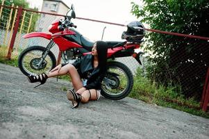 retrato de uma mulher legal e incrível na jaqueta de couro preta, sentado por uma bicicleta vermelha legal. foto