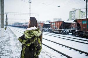 menina morena com casaco de pele verde na estação de plataforma em dia de inverno. foto