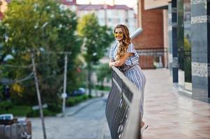 retrato de uma jovem perfeita usando óculos de sol listrados e amarelos posa na varanda de um edifício moderno em uma cidade. foto