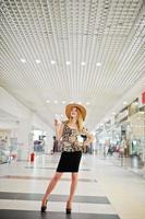 retrato de uma mulher de blusa de leopardo, saia preta posando no shopping com chapéu e uma xícara de café. foto