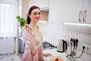 retrato de uma linda jovem de roupão rosa posando com salsa na mão. foto