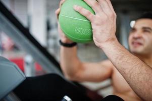 homem árabe musculoso treinando no ginásio moderno. homens árabes de fitness com torso nu fazendo exercícios com bola. foto