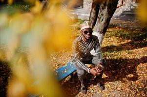 retrato de homem afro-americano elegante preto no chapéu e óculos de sol contra o fundo de outono ensolarado outono. pessoas ricas da áfrica em trajes tradicionais. foto