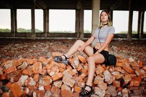 garota usa shorts na fábrica abandonada, sentado no tijolo. foto