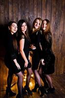 quatro amigas fofas usam vestidos pretos contra uma grande decoração de estrela de natal leve em fundo de madeira. foto