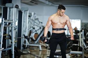 homem árabe musculoso treinando com halteres ginásio moderno. homens árabes de fitness com torso nu fazendo exercícios. foto