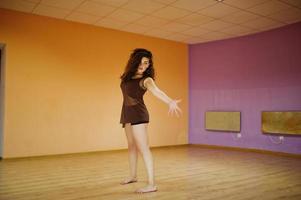 morena encaracolada mais modelo de tamanho fazendo acrobacias na sala de dança. foto