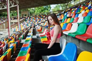 garota desportiva de fitness no sportswear sentado em esportes ao ar livre de cadeiras de estádio. mulher sexy feliz com maquete de garrafa de esporte. foto