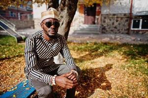 retrato de homem afro-americano elegante preto no chapéu e óculos de sol contra o fundo de outono ensolarado outono. pessoas ricas da áfrica em trajes tradicionais. foto