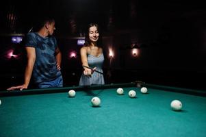 mulher de vestido jogando sinuca com um homem em um pub. foto