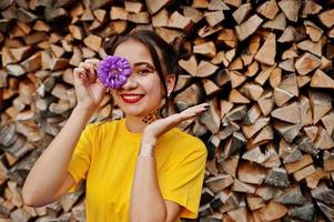 garota de camisa amarela com flores de áster violeta na mão atrás do olho. foto