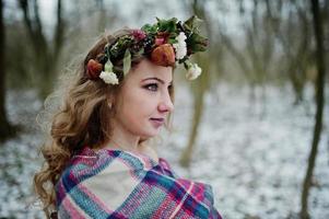 loira bonita encaracolada com coroa de flores em xadrez xadrez na floresta de neve em dia de inverno. foto