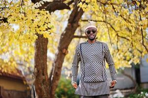 retrato de homem afro-americano elegante preto no chapéu e óculos de sol contra o fundo de outono ensolarado outono. pessoas ricas da áfrica em trajes tradicionais. foto