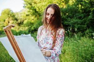 retrato de uma jovem atraente em vestido longo pintando com aquarela na natureza. foto