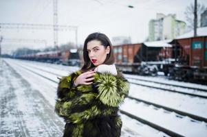 menina morena com casaco de pele verde na estação de plataforma em dia de inverno. foto