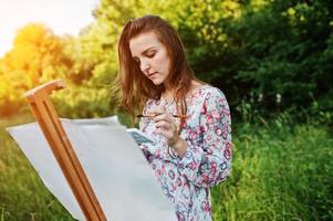 retrato de uma jovem atraente em vestido longo pintando com aquarela na natureza. foto