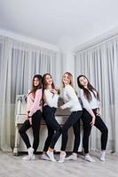 quatro amigas fofas usam blusas quentes e calças pretas contra piano velho com decoração de natal no quarto branco. foto
