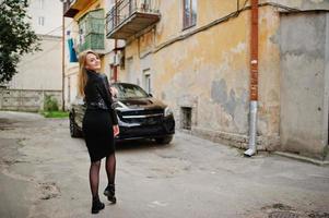 menina loira elegante usar jaqueta de couro preta posando nas ruas do carro de luxo de fundo da cidade. foto