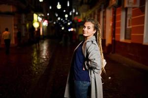 menina com dreadlocks andando na rua à noite da cidade. foto