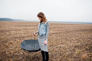 retrato de menina morena encaracolada na jaqueta jeans com guarda-chuva preto no campo. foto