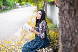 jovem sentada em um banco lendo um livro debaixo de uma bela árvore. foto