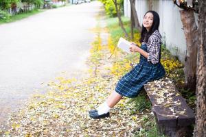 jovem sentada em um banco lendo um livro debaixo de uma bela árvore. foto