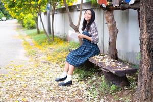 jovem sentada em um banco lendo um livro debaixo de uma bela árvore. foto