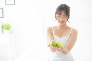 belo retrato jovem mulher asiática segurando e comendo fruta maçã verde no quarto em casa, estilo de vida de nutrição menina saudável e cuidados com o conceito de perda de peso, saúde e bem-estar. foto