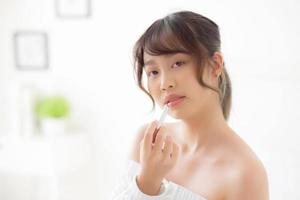belo retrato jovem mulher asiática aplicando batom de maquiagem no quarto, beleza lábios maquiagem menina Ásia e moda cosmética na boca em casa, estilo de vida e conceito de cuidados de saúde. foto