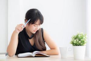 jovem escritora asiática sorrindo pensando a ideia e escrevendo no caderno ou diário com feliz no escritório, estilo de vida da garota asiática é sucesso, planejamento feminino de trabalho, educação e conceito de negócios. foto