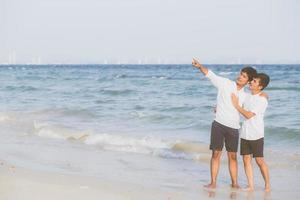 retrato homossexual jovem casal asiático em pé apontando algo juntos na praia no verão, ásia gay indo mar para lazer com romântico e feliz em férias no mar, lgbt com conceito legal. foto