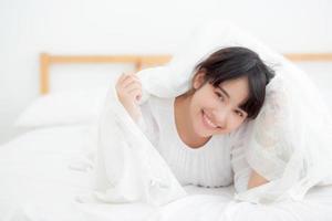 belo retrato jovem mulher asiática mentindo e sorria enquanto acorda com o nascer do sol de manhã, menina com feliz e divertido no quarto, estilo de vida e conceito de relaxamento. foto