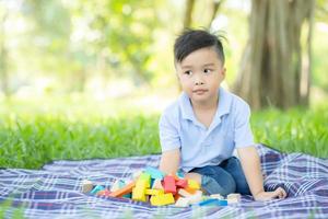 garotinho está jogando por ideia e inspiração com bloco de brinquedo no campo de grama, criança aprendendo com bloco de construção para educação, atividade infantil e jogo no parque com feliz no verão. foto