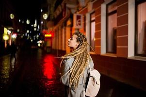 menina com dreadlocks andando na rua à noite da cidade. foto