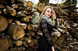 jovem loira de preto com cachecol posou contra fundo de tocos de madeira. foto