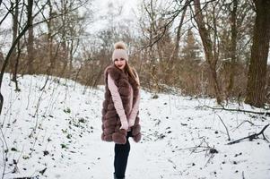 garota elegante com casaco de pele e chapéus na floresta de inverno. foto