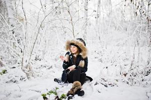 linda menina morena em roupas quentes de inverno. modelo de jaqueta de inverno e chapéu preto. foto