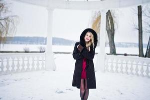 elegância loira com casaco de pele e vestido de noite vermelho posou em dia de inverno nevado. foto