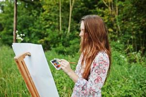 retrato de uma jovem atraente em vestido longo pintando com aquarela na natureza. foto