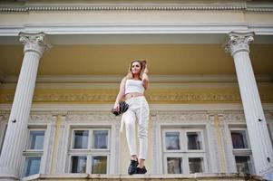 menina elegante modelo loira encaracolada usar branco posando contra a velha casa vintage. foto