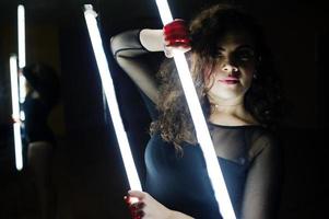 morena encaracolada modelo plus size com duas lâmpadas led longas na sala de dança com espelho. foto