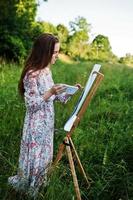 retrato de uma jovem atraente em vestido longo pintando com aquarela na natureza. foto