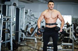 homem árabe musculoso treinando com halteres ginásio moderno. homens árabes de fitness com torso nu fazendo exercícios. foto