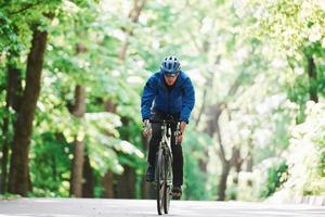 direto. ciclista de bicicleta está na estrada de asfalto na floresta em dia ensolarado foto